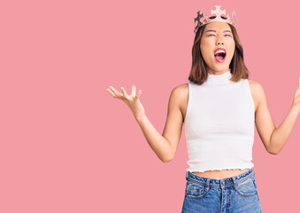 Young beautiful chinese girl wearing princess crown crazy and mad shouting and yelling with aggressive expression and arms raised. frustration concept. © Krakenimages.com