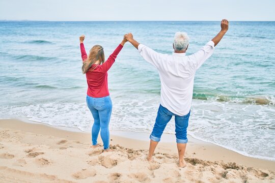 Middle age hispanic couple breathing with arms raised at the beach.