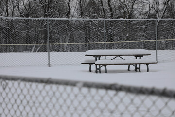 Winter snow gray afternoon day with outdoor picnic table and bench between wire fences