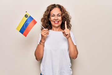 Middle age beautiful tourist woman holding venezuelan flag over isolated white background smiling with an idea or question pointing finger with happy face, number one