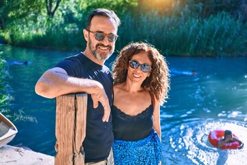 Middle age couple wearing casual clothes smiling happy. Standing looking at the camera hugging around river at park