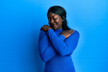 African young woman wearing casual clothes hugging oneself happy and positive, smiling confident....