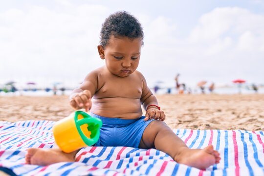 Adorable african american toddler playing with toys sitting on the sand at the beach.