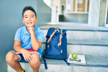 Adorable student boy smiling happy sitting on the stairs at school.