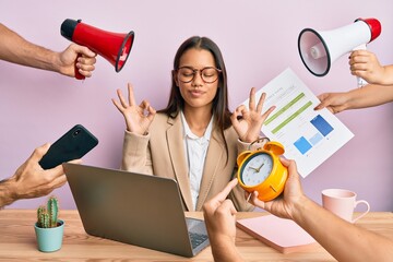 Beautiful hispanic woman working at the office under stress relax and smiling with eyes closed doing meditation gesture with fingers. yoga concept.