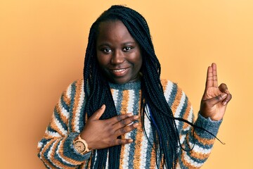 Young black woman with braids wearing casual winter sweater smiling swearing with hand on chest and...