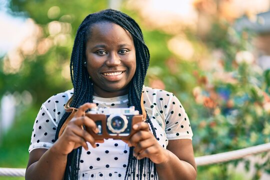 Young african american tourist woman smiling happy using vintage camera at the city.