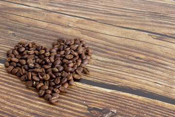 Coffee beans are placed in a heart shape with a wooden backdrop and can be used as a background.