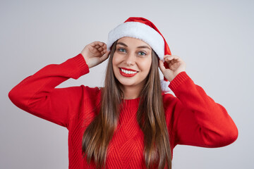 Cheerful young girl in a red sweater and Santa hat. Studio shot on gray background.