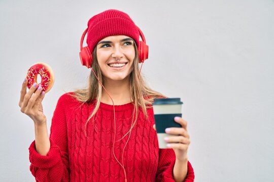 Young hispanic woman having breakfast using headphones at the city.