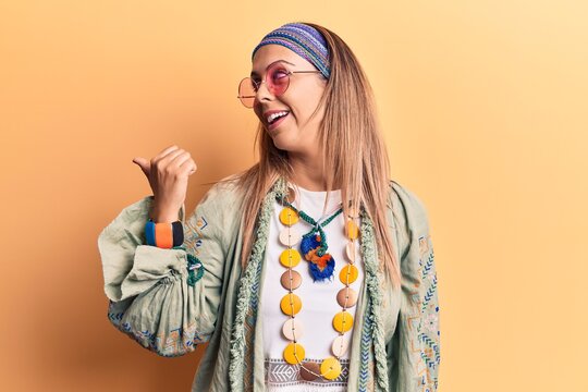 Young beautiful woman wearing hippi clothes pointing thumb up to the side smiling happy with open mouth