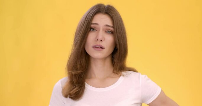 Young woman looking at camera with grading, but shaking head in denial, orange studio background, close up