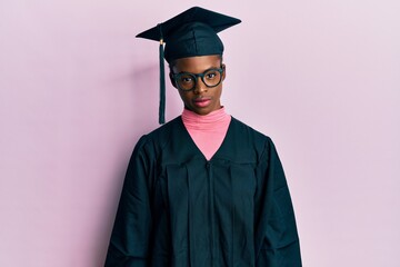 Young african american girl wearing graduation cap and ceremony robe relaxed with serious expression on face. simple and natural looking at the camera.