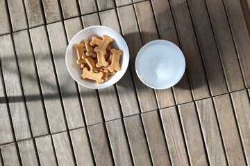 dry dog food and water in bowl on wooden background top view
