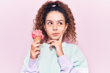 Beautiful kid girl with curly hair holding ice cream serious face thinking about question with hand...