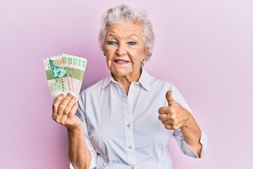 Senior grey-haired woman holding hong kong 50 dollars banknotes smiling happy and positive, thumb up doing excellent and approval sign