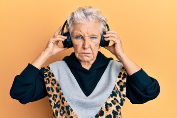 Senior grey-haired woman listening to music using headphones depressed and worry for distress,...