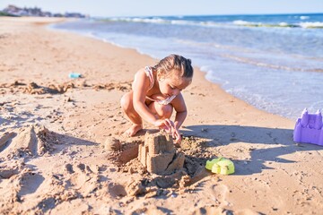 Fototapeta na wymiar Adorable blonde child wearing bikini. Building sand castle using bucket and shovel at the beach