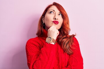 Young beautiful redhead woman wearing red casual turtleneck sweater over pink background thinking...