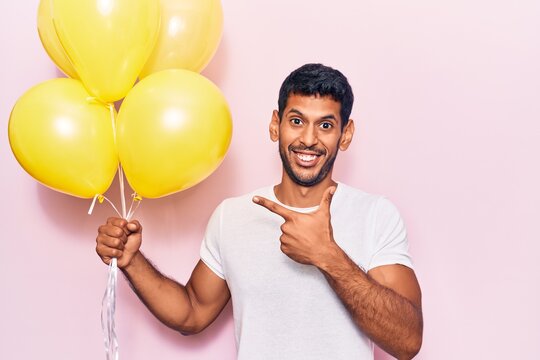 Young latin man holding balloons smiling happy pointing with hand and finger