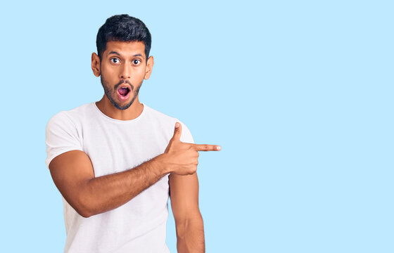 Young latin man wearing casual clothes surprised pointing with finger to the side, open mouth amazed expression.