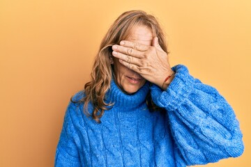 Middle age blonde woman wearing glasses and casual winter sweater smiling and laughing with hand on face covering eyes for surprise. blind concept.