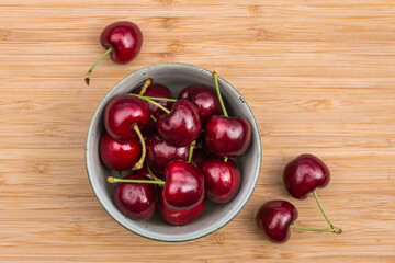 closeup of ripe Stella cherries in porcelain bowl on bamboo chopping board with copy space