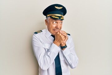 Handsome middle age mature man wearing airplane pilot uniform laughing nervous and excited with hands on chin looking to the side