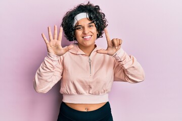 Young hispanic woman with curly hair wearing sportswear showing and pointing up with fingers number...