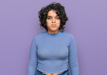 Young hispanic woman with curly hair wearing casual clothes puffing cheeks with funny face. mouth...