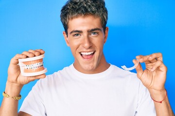 Young handsome man holding orthodontic smiling and laughing hard out loud because funny crazy joke.