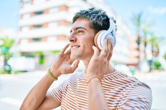 Young handsome caucasian man smiling happy listening to music using headphones walking at city.