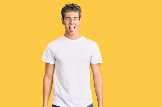 Young handsome man wearing casual white tshirt sticking tongue out happy with funny expression. emotion concept.
