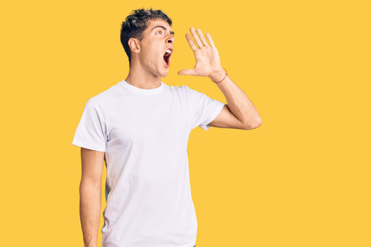 Young handsome man wearing casual white tshirt shouting and screaming loud to side with hand on mouth. communication concept.