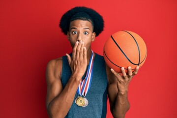African american man with afro hair wearing winner medals at basketball player covering mouth with hand, shocked and afraid for mistake. surprised expression - Powered by Adobe