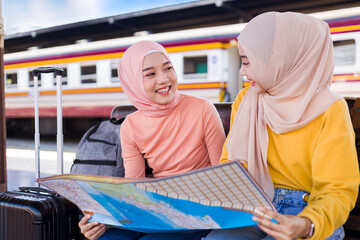 Two Muslim women looked at the map and smiled happily as they waited for the train at the platform.