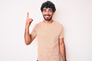 Handsome young man with curly hair and bear wearing casual striped tshirt pointing finger up with successful idea. exited and happy. number one.