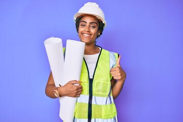 Young african american woman with braids wearing safety helmet holding blueprints smiling happy and positive, thumb up doing excellent and approval sign