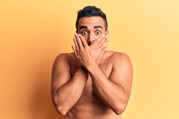 Young hispanic man standing shirtless shocked covering mouth with hands for mistake. secret concept.