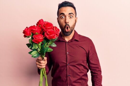 Young hispanic man holding flowers scared and amazed with open mouth for surprise, disbelief face