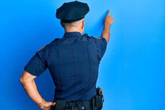 Middle age handsome man wearing police uniform posing backwards pointing ahead with finger hand