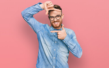 Young redhead man wearing casual denim shirt smiling making frame with hands and fingers with happy...