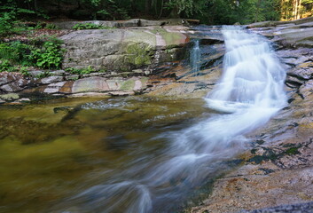 Bottom view of a river with waterfalls falling down in a forest, rocks are all around