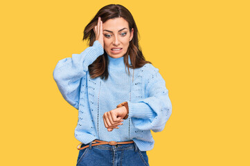 Young brunette woman wearing casual winter sweater looking at the watch time worried, afraid of...