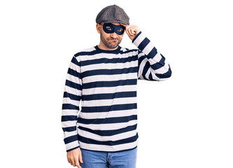 Young handsome man wearing burglar mask worried and stressed about a problem with hand on forehead, nervous and anxious for crisis