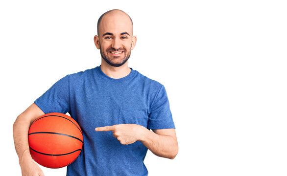 Young handsome man holding basketball ball smiling happy pointing with hand and finger
