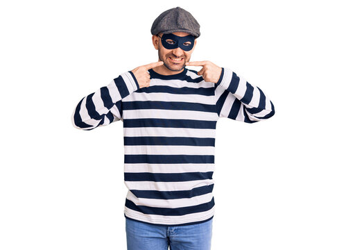 Young handsome man wearing burglar mask smiling cheerful showing and pointing with fingers teeth and mouth. dental health concept.