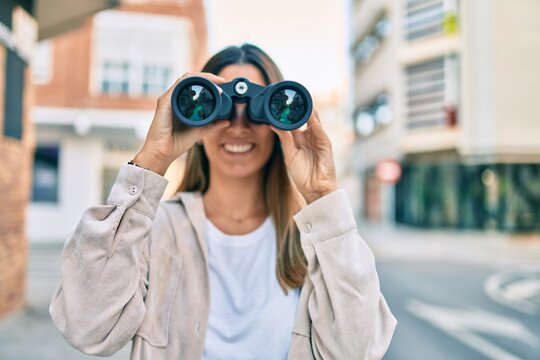 Young caucasian woman smiling happy looking for new opportunity using binoculars walking at the city.