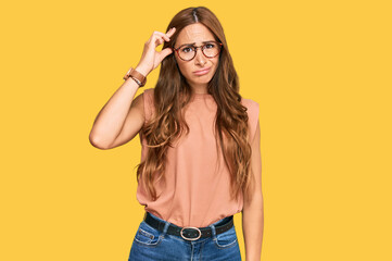 Young hispanic woman wearing casual clothes and glasses worried and stressed about a problem with hand on forehead, nervous and anxious for crisis