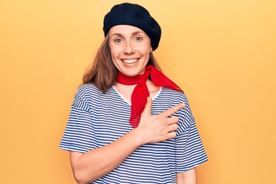 Young beautiful blonde woman wearing french fashion style with scarf and beret smiling cheerful pointing with hand and finger up to the side